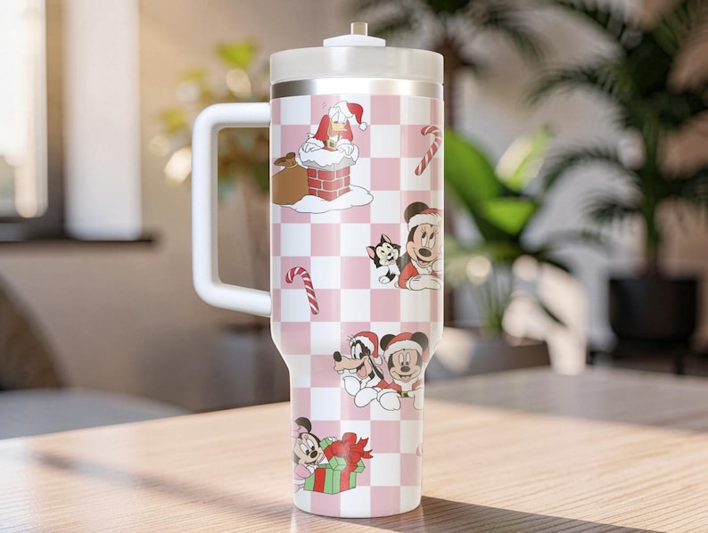 May include: A white and pink insulated tumbler with a handle, featuring a Christmas-themed design. The tumbler is decorated with cartoon characters, candy canes, and Santa Claus. The design is set against a checkered background.