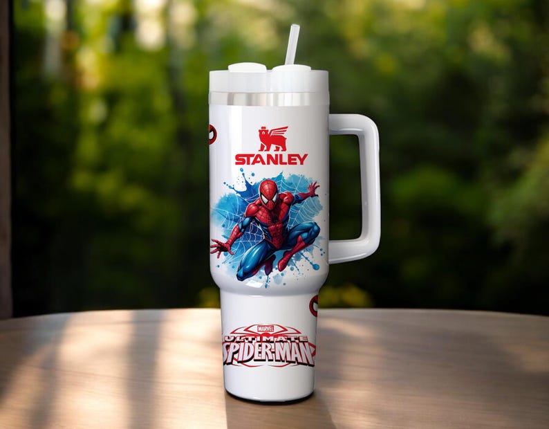 Puede incluir: Vaso Stanley blanco con un dise&ntilde;o de Spider-Man. El vaso tiene un asa, una tapa blanca con pajita y el logotipo de Marvel Ultimate Spider-Man. El dise&ntilde;o incluye una ilustraci&oacute;n de Spider-Man rojo y azul sobre un fondo de salpicaduras azules.