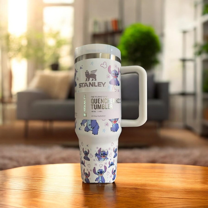 K&ouml;nnte beinhalten: Wei&szlig;er Stanley Quencher H2.0 Becher mit Griff, mit einem Cartoon-Charakter-Design. Der Becher hat ein Fassungsverm&ouml;gen von 1,18 L und enth&auml;lt den Text "The Flowstate" und "All Day Hydration".