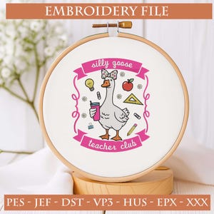 May include: An embroidery hoop with a white fabric featuring a cartoon goose design. The goose wears a bow and holds a drink. The text "silly goose teacher club" is displayed on a pink banner. The words "EMBROIDERY FILE" are at the top.