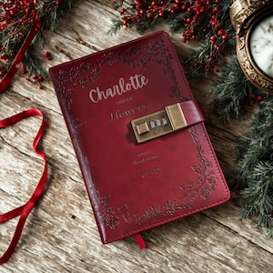 Puede incluir: Un diario de cuero burdeos con el nombre "Charlotte" y las palabras "Vintage Flowers" grabadas. Cuenta con un candado de combinación y un diseño floral. Se ve una cinta roja como marcapáginas.