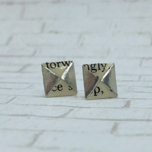 May include: A pair of silver earrings with a square shape. Each earring is made from a folded piece of paper with text printed on it. The text on the left earring reads "torw ce s" and the text on the right earring reads "ngly p,".