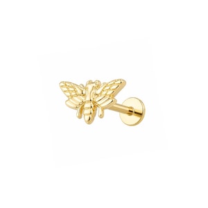 May include: A gold-toned bee-shaped stud earring featuring a flat circular backing and a post. The bee design includes detailed wings with a grid-like texture and a segmented body, all rendered in a polished, reflective metallic gold finish.