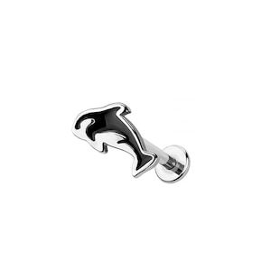 May include: A silver lip piercing with a black and silver dolphin design. The dolphin is depicted in a stylized form with a curved body. The piercing has a flat back and a straight post.