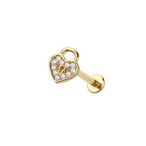 May include: A gold lip piercing stud with a heart-shaped padlock design. The heart is set with small, clear gemstones. The stud has a straight post and a flat, round backing.