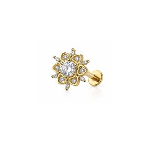 Può includere: Un piercing labret color oro con retro piatto, caratterizzato da una pietra centrale rotonda trasparente circondata da una disposizione floreale di cornici dorate a forma di cuore, ognuna contenente una piccola pietra trasparente.