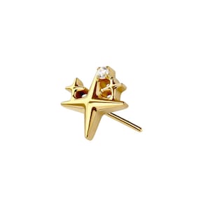 May include: A gold-colored stud earring in the shape of a star with a small, clear gemstone at the center. The earring has a post for insertion into the ear and is set against a white background.