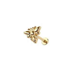 May include: A gold-colored bee-shaped earring stud. The bee has detailed wings and body segments. The earring post and backing are also gold. The jewelry is set against a white background.