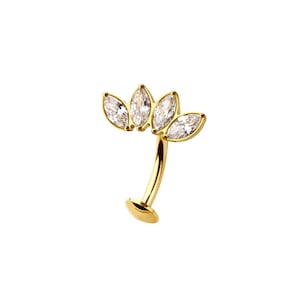 Puede incluir: Una joya corporal curva de color dorado con cuatro piedras preciosas claras con corte marquesa dispuestas en un patrón floral. La joya tiene un tallo curvo y una base plana, diseñada para piercings.