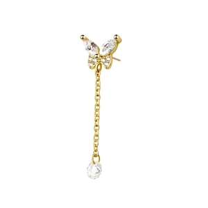 May include: A gold-colored butterfly earring with a dangling chain and a teardrop-shaped gem. The butterfly design features clear, sparkling stones. The earring is set against a white background.