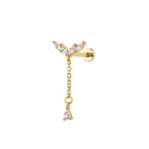 Può includere: Un orecchino color oro con un design decorativo. L'orecchino presenta un gruppo di pietre chiare e scintillanti nella parte superiore, una delicata catena e un'unica pietra a forma di goccia all'estremità. L'orecchino è progettato per essere indossato in un piercing.