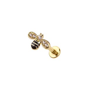 May include: A gold-colored lip piercing featuring a bee design. The bee has black and gold stripes on its body and clear, sparkling accents on its wings. The piercing has a flat back for comfortable wear.