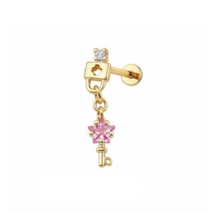 Könnte beinhalten: Goldfarbener Ohrring mit einem kleinen Schloss-Design und einem Anhänger in Form eines Schlüssels. Der Schlüsselanhänger hat einen rosa sternförmigen Edelstein und einen kleinen Schlüssel. Auf der Oberseite des Ohrrings ist ein kleiner klarer Edelstein gesetzt.