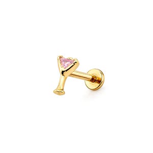 May include: A gold-colored lip piercing stud shaped like a martini glass. The martini glass has a pink, heart-shaped gem in the glass. The stud has a flat back and a straight post for insertion.