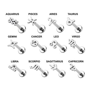 May include: A collection of twelve silver-toned metal labret studs, each featuring a unique zodiac sign symbol. The signs include Aquarius, Pisces, Aries, Taurus, Gemini, Cancer, Leo, Virgo, Libra, Scorpio, Sagittarius, and Capricorn.