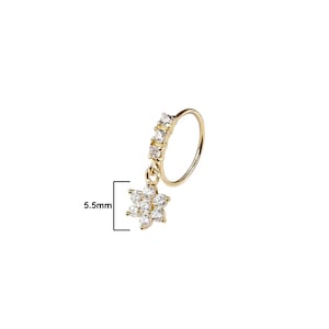 May include: A gold-colored nose ring with a dangling flower pendant. The ring features a row of four clear, square-cut stones and a flower pendant with multiple clear stones. The pendant measures 5.5mm.