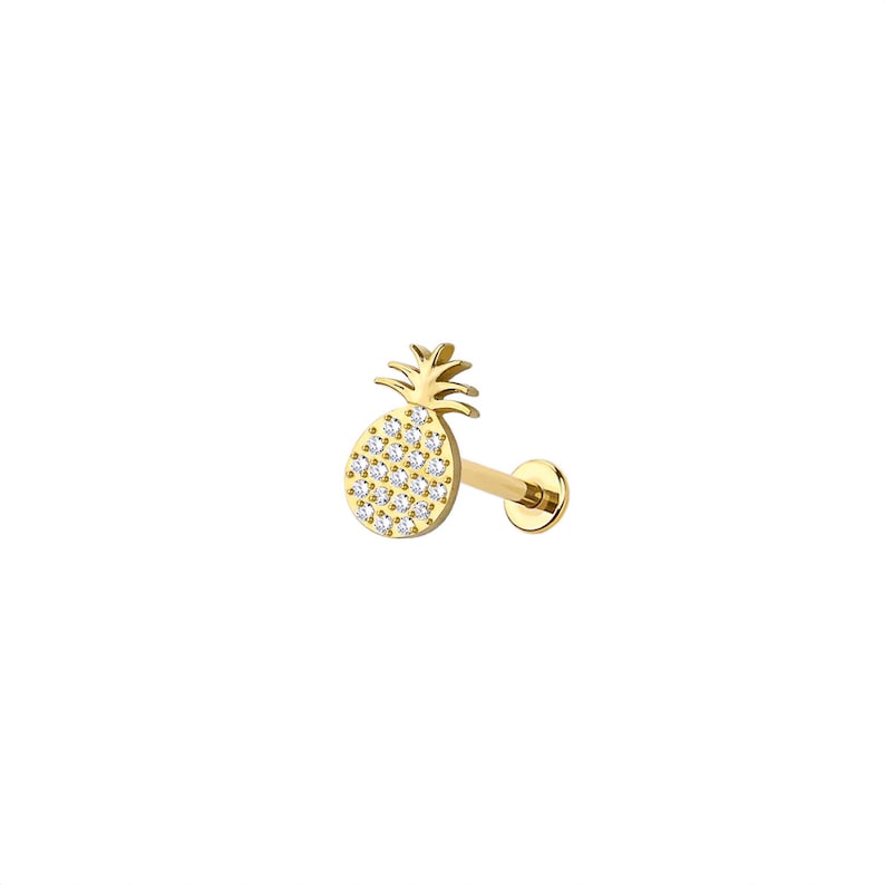 May include: A gold-colored, pineapple-shaped stud earring with a flat back. The pineapple is encrusted with small, clear gemstones. The earring post is a straight, gold-colored bar. The earring is set against a white background.