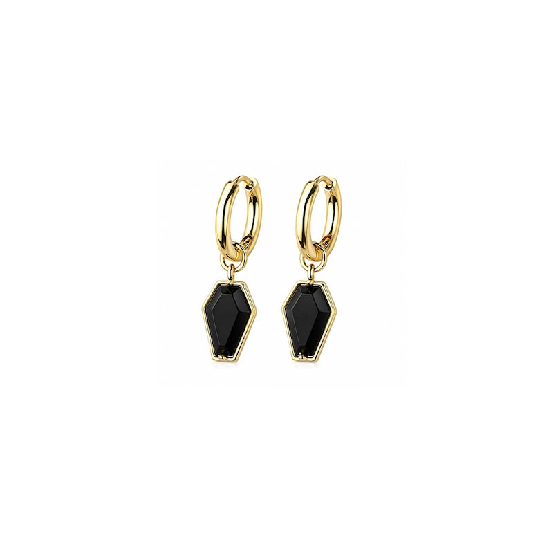 May include: A pair of gold-toned hoop earrings featuring dangling coffin-shaped charms. Each charm is crafted with a polished gold metal frame surrounding a smooth, solid black inlay. The earrings utilize a hinged closure mechanism for secure wear.
