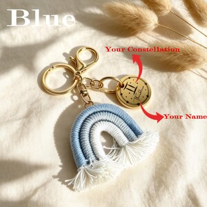 Pode incluir: Um porta-chaves de metal dourado com um arco-íris de macramé em tons de azul e branco com extremidades em franjas. Inclui um pendente circular de metal dourado gravado com o símbolo do signo Gémeos e o nome Theodora em texto preto.