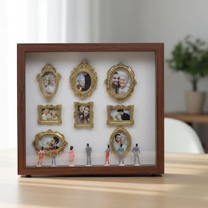 Może przedstawiać: Brązowe drewniane pudełko z dziewięcioma małymi, ozdobnymi, złotymi ramkami na zdjęcia, z których każda zawiera fotografię. Miniaturowe figurki są umieszczone pod ramkami. Pudełko stoi na drewnianym stole.