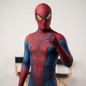 May include: A full-body spandex costume featuring a red and blue color scheme with a textured honeycomb pattern. The suit includes a matching mask with large, white, reflective eye lenses and a black spider emblem centered on the chest area.