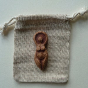 Puede incluir: Una peque&ntilde;a figurita de cer&aacute;mica marr&oacute;n de una mujer con la cabeza y los brazos levantados. La figurita est&aacute; sentada en una peque&ntilde;a bolsa de cord&oacute;n beige.