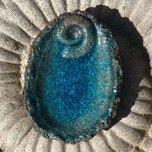 Könnte beinhalten: Eine handgefertigte, ovale Keramikschale mit leuchtend türkisfarbener Glasur und einer strukturierten, rissigen Oberfläche. Die Schale hat ein Spiraldesign in der Mitte und einen dunklen, strukturierten Rand. Die Schale steht auf einer strukturierten, grauen Oberfläche.
