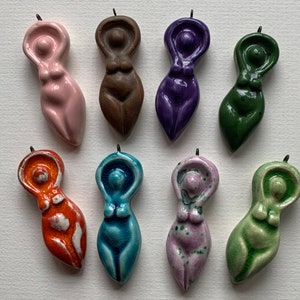 May include: Ten ceramic figurines of a female figure in various colours, including pink, brown, purple, green, orange, blue, and light green. Each figurine has a loop at the top for hanging.