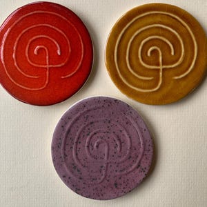 Peut inclure: Trois dessous de verre ronds en céramique, rouges, dorés et violets. Chaque dessous de verre présente un motif en spirale. Ces dessous de verre protègent les surfaces des boissons chaudes ou froides. Un article décoratif et fonctionnel.