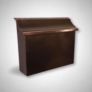 May include: A bronze-colored mailbox with a curved top and a rectangular body. The mailbox has a dark, metallic finish and a simple, elegant design. The top edge has a lighter bronze trim.