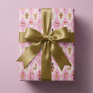Könnte beinhalten: Ein rechteckiges Geschenkpaket in hellrosa Papier mit weißem Rautenmuster, das mit kleinen Weihnachtssymbolen wie dem Weihnachtsmann, Nussknackern, Lebkuchenmännern, Zuckerstangen und Tannenbäumen bedruckt und mit einem goldenen Satinband verziert ist.