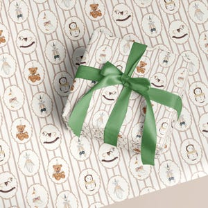 May include: Gift-wrapped present with a green satin bow, placed on a matching patterned wrapping paper. The paper features a repeating pattern of oval frames with toy illustrations and vertical stripes.