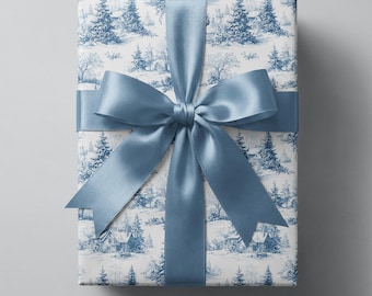 Puede incluir: Una caja de regalo rectangular envuelta en papel blanco con un patrón de paisaje invernal azul estilo toile, que muestra pinos y casas. El paquete está atado con una cinta de satén ancha y lisa de color azul ceniza en un gran lazo central.