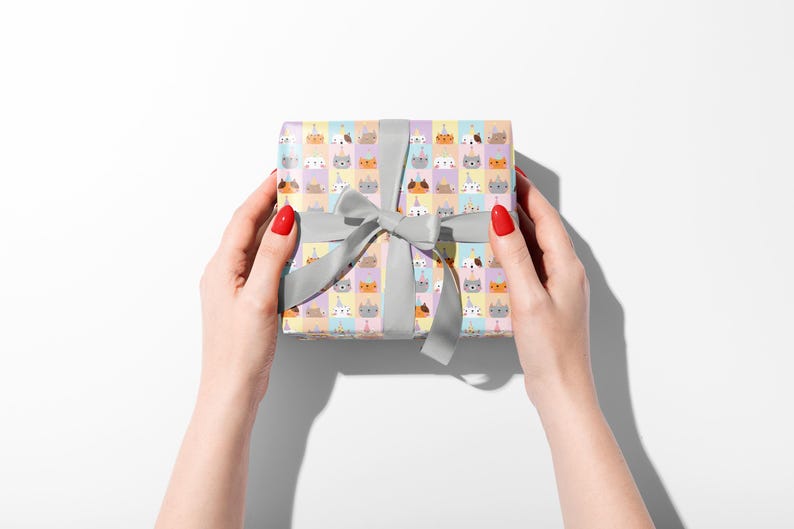 May include: A gift box wrapped in patterned paper with cartoon animal faces, including cats and unicorns, is held by two hands. The box is tied with a grey ribbon and bow. The background is white.