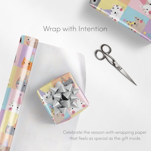 May include: A wrapped gift with a cat face pattern and a silver bow. A roll of matching wrapping paper and scissors are also present. Text reads: "Wrap with Intention" and "Celebrate the season with wrapping paper that feels as special as the gift inside."