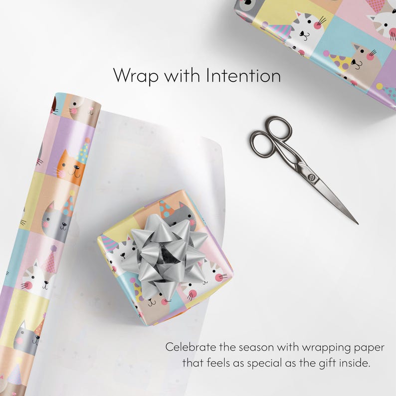 May include: A wrapped gift with a cat face pattern and a silver bow. A roll of matching wrapping paper and scissors are also present. Text reads: "Wrap with Intention" and "Celebrate the season with wrapping paper that feels as special as the gift inside."