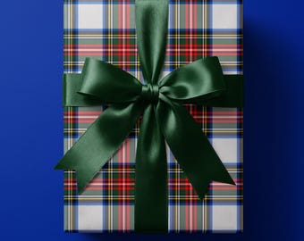 May include: A rectangular gift box wrapped in white paper featuring a multi-colored plaid pattern of red, green, blue, and yellow lines. The package is tied with a wide, smooth, dark forest green satin ribbon arranged in a large decorative bow.