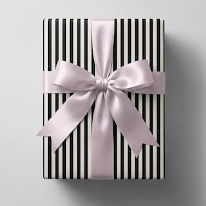 May include: A rectangular gift box wrapped in paper featuring a pattern of vertical black and white stripes. The box is tied with a wide, smooth, light lavender satin ribbon that is tied into a large, centred bow with two long tails.