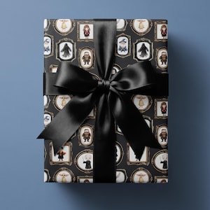 Puede incluir: Una caja de regalo rectangular envuelta en papel gris oscuro con un patrón repetitivo de pequeños personajes de fantasía ilustrados dentro de marcos dorados ornamentados. Una cinta de satén negra ancha y lisa forma un gran lazo central.