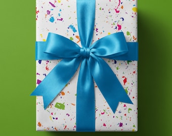 May include: A rectangular gift box wrapped in white paper featuring a multi-colored paint splatter pattern in shades of blue, green, yellow, orange, and pink. The box is tied with a wide, smooth, bright blue satin ribbon tied in a large bow.