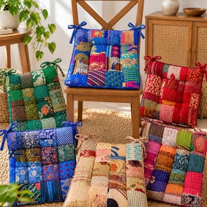 Puede incluir: Una colección de seis cojines de asiento cuadrados con diseños de patchwork hechos de varias telas coloridas con costuras kantha visibles. Cada cojín incluye lazos de tela en las esquinas superiores para sujetarlo a una silla, mostrando diversos patrones en tonos azules, verdes, rojos y neutros.
