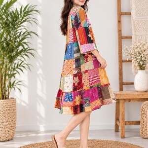May include: A knee-length dress featuring a vibrant patchwork design with various colorful fabric squares in shades of red, yellow, blue, and pink, finished with a ruffled hem and three-quarter length sleeves.