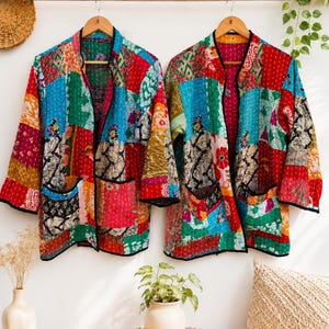 May include: Two long-sleeved jackets featuring a patchwork design of various colourful fabrics in shades of red, blue, green, and yellow. Each jacket has a mandarin collar, black trim along the edges, and two front pockets with visible stitching.