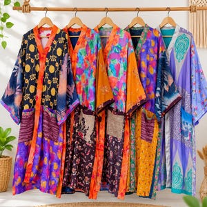 May include: Five long-sleeved robes hanging on a wooden rack, each featuring distinct vibrant patterns, floral motifs, and patchwork designs in various colors including orange, purple, yellow, blue, and black, with visible front pockets.