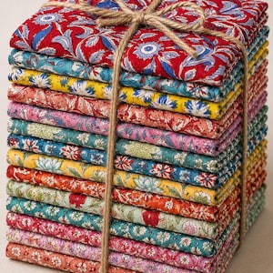 May include: A stack of folded fabric squares featuring various floral and botanical patterns in vibrant colours including red, yellow, pink, teal, and green. The fabric bundle is tied together with a simple brown jute twine tied in a bow.