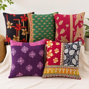 May include: Five square throw pillows featuring kantha stitching. One is black with red and tan leaves, one green with paisley, one pink with tan leaves, one purple with pink floral motifs, and one with red, yellow, and black floral patterns.