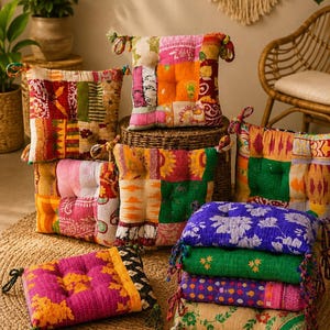 May include: A collection of square floor cushions featuring various patchwork designs with vibrant colors including pink, orange, green, yellow, and blue. Each cushion has tufted details and fabric ties at the corners, arranged in a stack and pile.