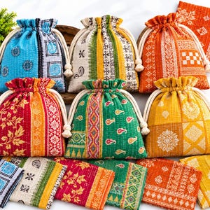 Op de afbeelding: Een collectie van zes stoffen buidels met trekkoord en bijpassende gevouwen stoffen vierkanten met levendige, veelkleurige patronen, waaronder bloem-, geometrische en paisley-ontwerpen in tinten blauw, groen, geel, oranje en rood.