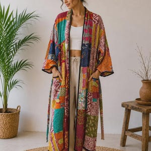 May include: A long, open-front kimono robe featuring a vibrant patchwork design with various colourful fabric squares in shades of red, orange, yellow, blue, and green. The garment includes long sleeves, two front pockets, and black trim.