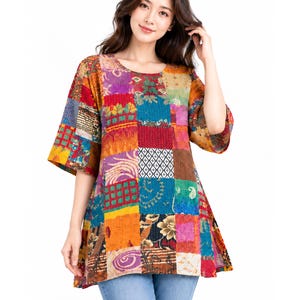 May include: A short-sleeved tunic featuring a vibrant patchwork design with various colorful patterns including floral, geometric, and abstract motifs in shades of red, orange, yellow, blue, and purple, paired with light blue denim jeans.